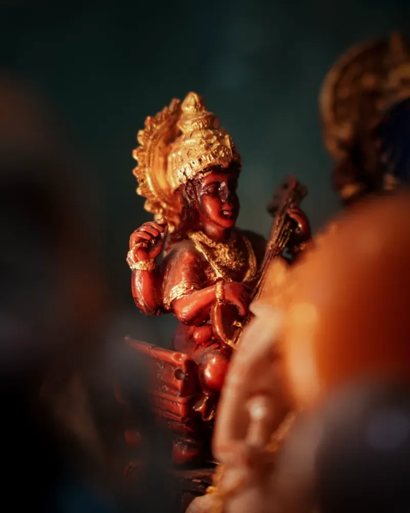 A small painted figurine of a crowned deity holding a stringed instrument, in warm light during a festival