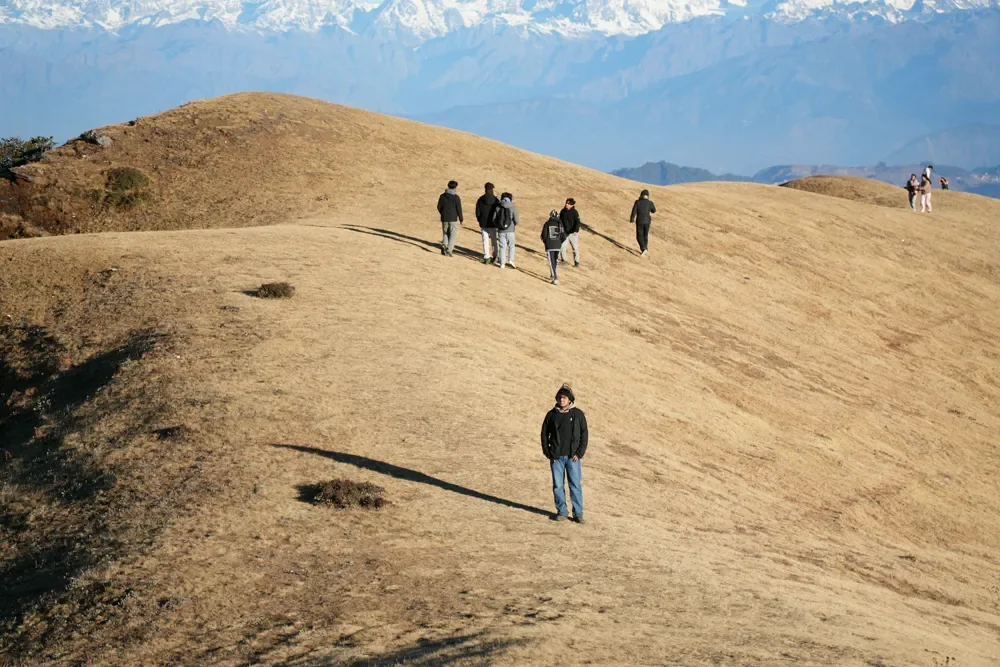 Hikers walk along a golden, grass-covered ridgeline with a hazy snow-capped range in the distance at Sailung